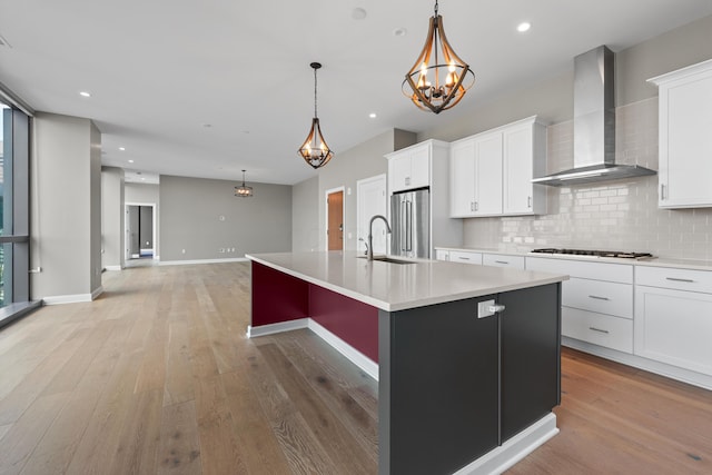 kitchen with a sink, high end fridge, wall chimney range hood, light wood-type flooring, and tasteful backsplash