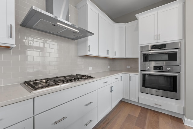 kitchen featuring dark wood finished floors, light countertops, decorative backsplash, appliances with stainless steel finishes, and wall chimney range hood