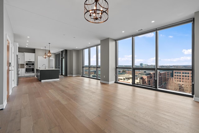 unfurnished living room featuring a chandelier, baseboards, floor to ceiling windows, and light wood finished floors