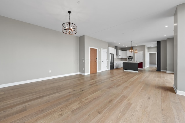 unfurnished living room featuring light wood-style floors, recessed lighting, a notable chandelier, and baseboards