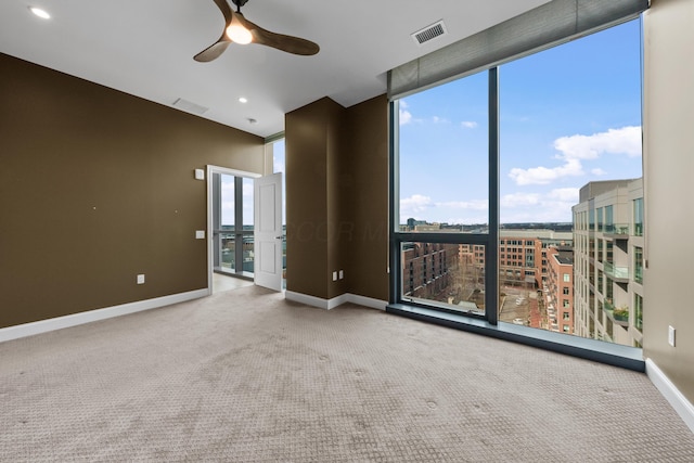 spare room with carpet floors, a ceiling fan, visible vents, baseboards, and a wall of windows