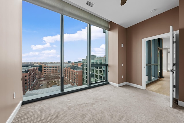 carpeted empty room featuring expansive windows, a city view, visible vents, and baseboards