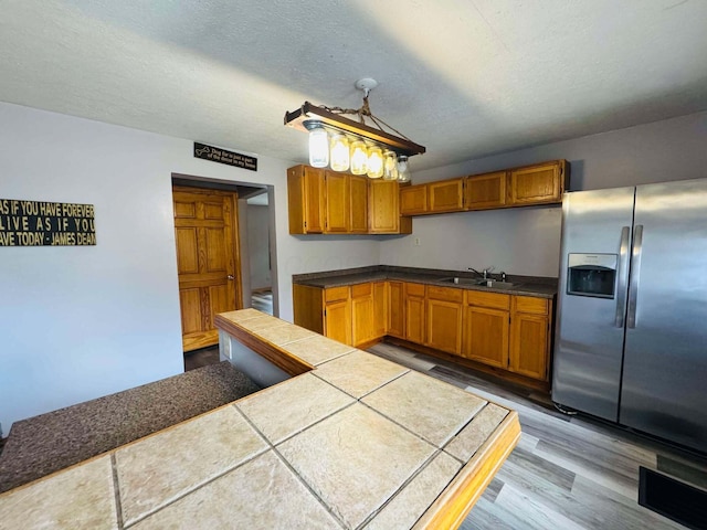 kitchen with stainless steel refrigerator with ice dispenser, a textured ceiling, sink, hardwood / wood-style flooring, and tile counters