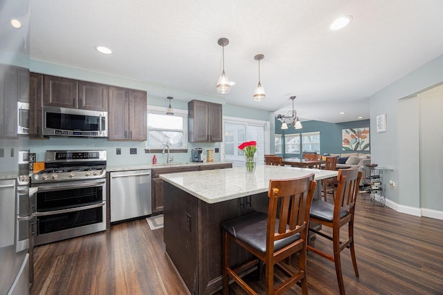 kitchen featuring pendant lighting, a center island, dark wood-type flooring, light stone countertops, and stainless steel appliances