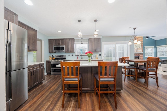 kitchen featuring dark hardwood / wood-style flooring, stainless steel appliances, sink, decorative light fixtures, and a kitchen island