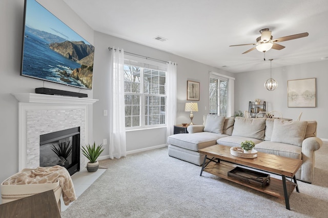 living room featuring ceiling fan with notable chandelier, a stone fireplace, and light carpet