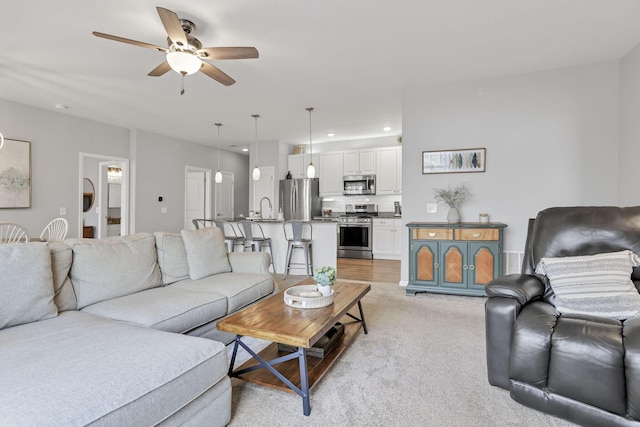 carpeted living room with ceiling fan and sink