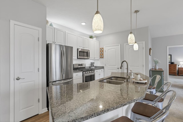 kitchen featuring white cabinets, sink, dark stone countertops, appliances with stainless steel finishes, and decorative light fixtures