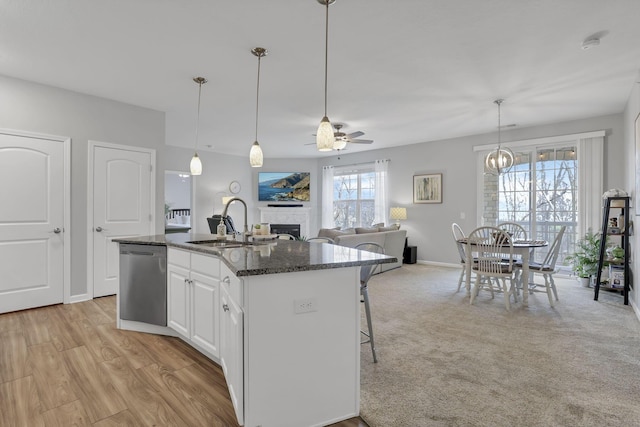 kitchen with white cabinetry, dishwasher, ceiling fan, dark stone counters, and a kitchen island with sink