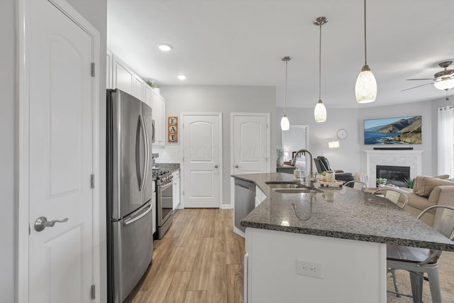 kitchen featuring stainless steel appliances, sink, white cabinetry, hanging light fixtures, and a breakfast bar area