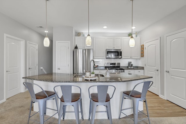 kitchen featuring a kitchen island with sink, white cabinets, stainless steel appliances, and decorative light fixtures