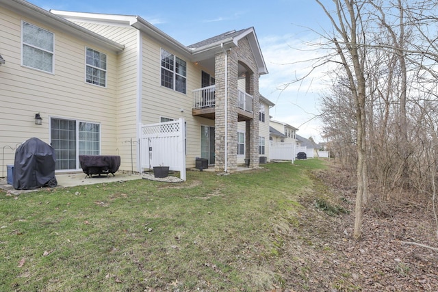 rear view of property with a balcony, cooling unit, and a lawn