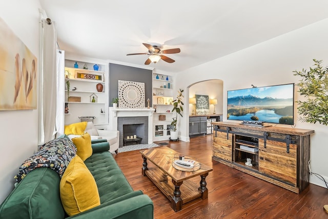 living room with built in shelves, ceiling fan, dark hardwood / wood-style flooring, and a brick fireplace