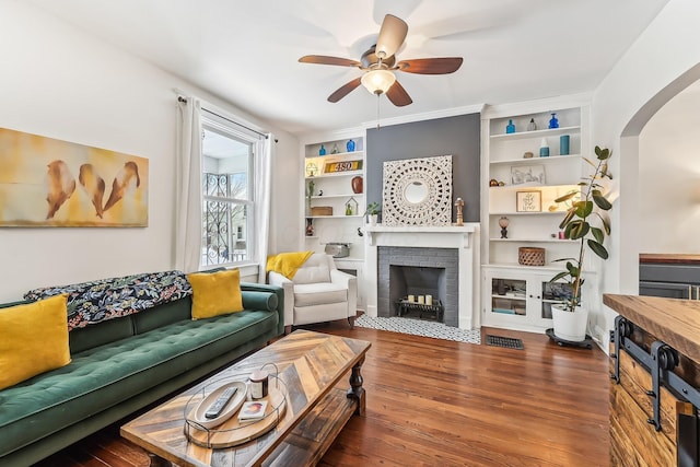 living room featuring built in shelves, ceiling fan, wood-type flooring, and a fireplace