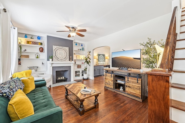 living room featuring dark hardwood / wood-style flooring, a brick fireplace, built in features, and ceiling fan