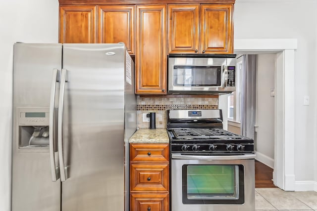 kitchen with light stone counters, stainless steel appliances, light tile patterned floors, and backsplash