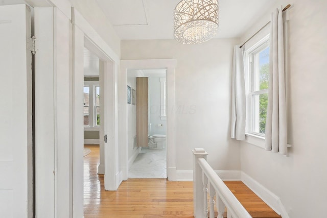 corridor with light wood-type flooring, baseboards, a chandelier, and an upstairs landing