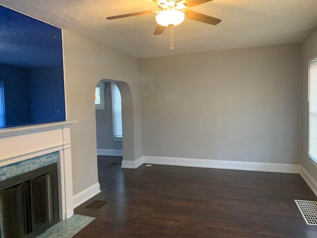 unfurnished living room with a textured ceiling, ceiling fan, dark wood-type flooring, and a tiled fireplace