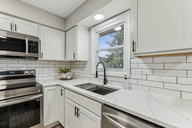 kitchen featuring white cabinets, sink, appliances with stainless steel finishes, tasteful backsplash, and light stone counters