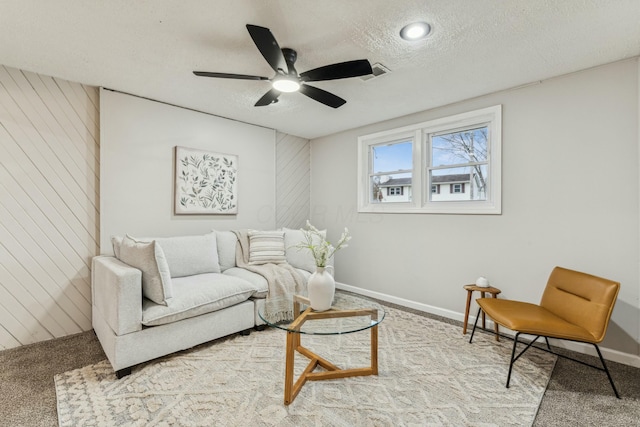 carpeted living room featuring ceiling fan, wood walls, and a textured ceiling