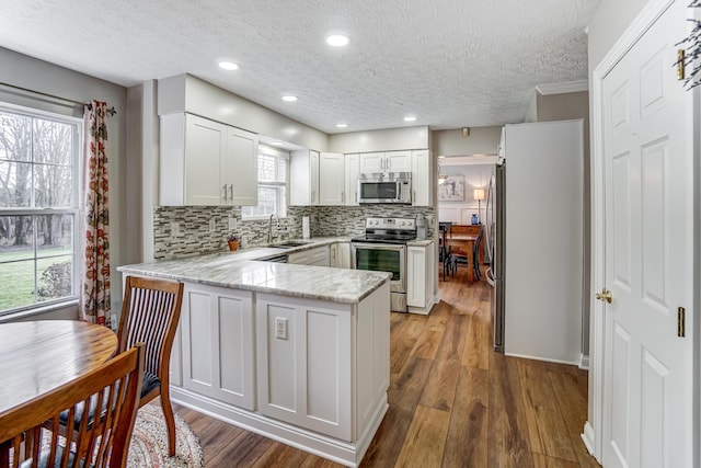 kitchen featuring white cabinetry, sink, backsplash, kitchen peninsula, and appliances with stainless steel finishes