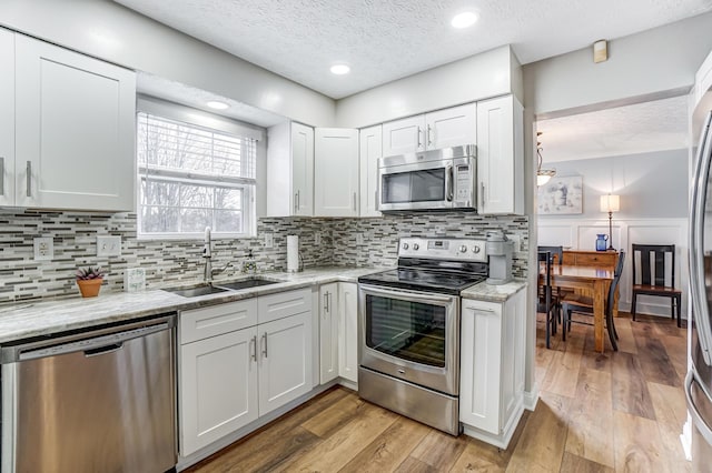 kitchen featuring appliances with stainless steel finishes, light hardwood / wood-style floors, white cabinetry, and sink