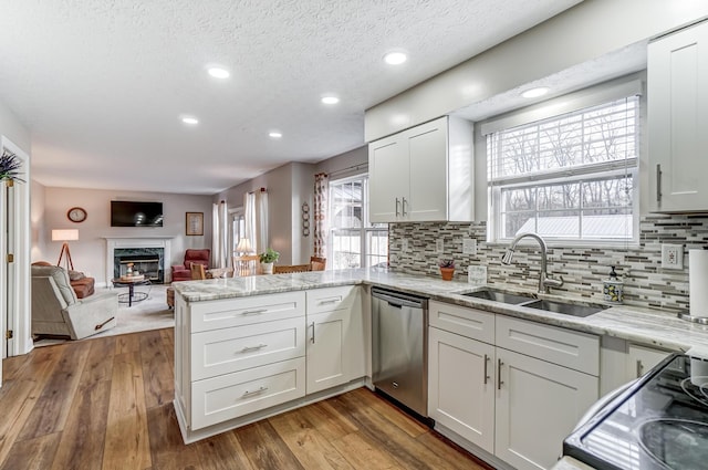 kitchen with kitchen peninsula, a high end fireplace, sink, dishwasher, and white cabinetry