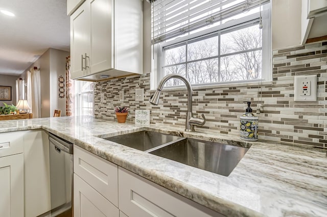 kitchen featuring dishwasher, backsplash, white cabinets, sink, and light stone countertops