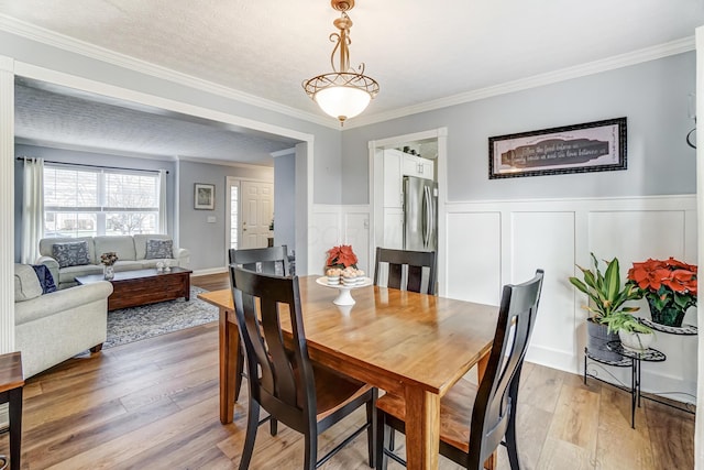 dining space with light hardwood / wood-style floors, ornamental molding, and a textured ceiling