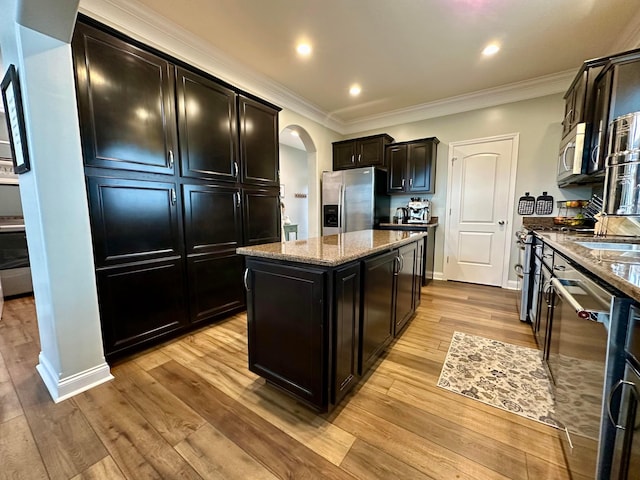 kitchen featuring a kitchen island, light stone counters, ornamental molding, and appliances with stainless steel finishes