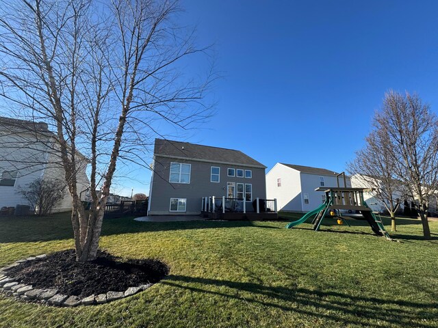 rear view of property with a playground, a yard, and a deck