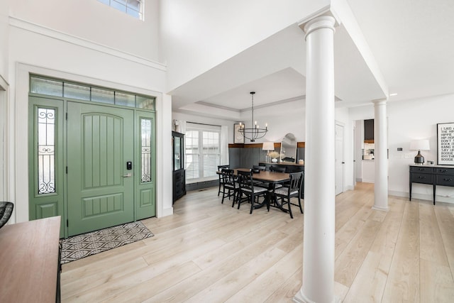 entryway featuring a notable chandelier, light hardwood / wood-style floors, a raised ceiling, and ornate columns