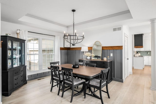 dining area with a chandelier, ornamental molding, a raised ceiling, and light wood-type flooring