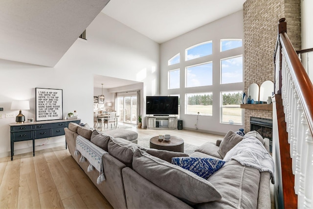 living room with a brick fireplace, a towering ceiling, and light hardwood / wood-style flooring