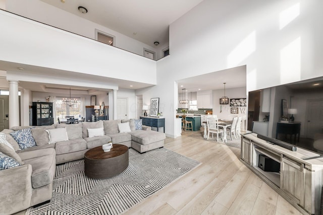 living room featuring decorative columns, a high ceiling, a chandelier, and light hardwood / wood-style floors