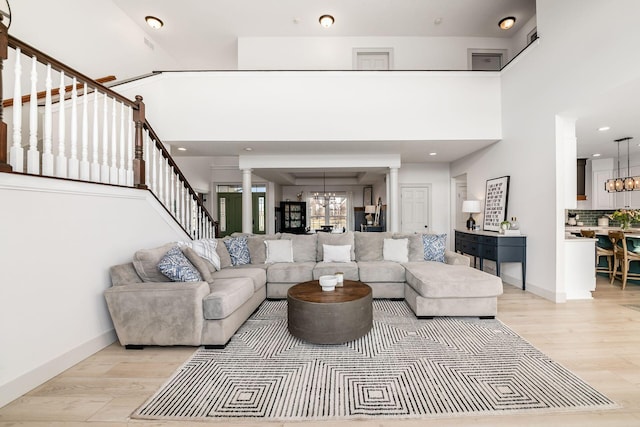 living room featuring decorative columns, a high ceiling, an inviting chandelier, and light hardwood / wood-style floors