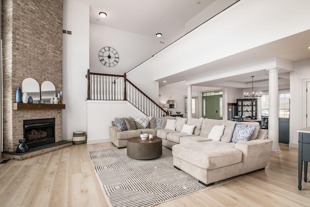 living room with a fireplace, decorative columns, a chandelier, a high ceiling, and light wood-type flooring