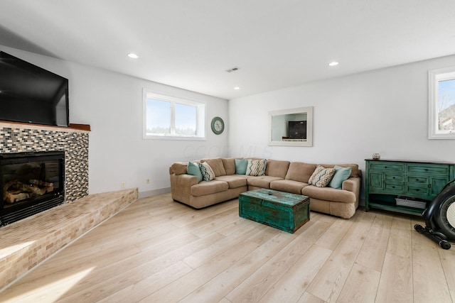 living room with a tiled fireplace, plenty of natural light, and light wood-type flooring