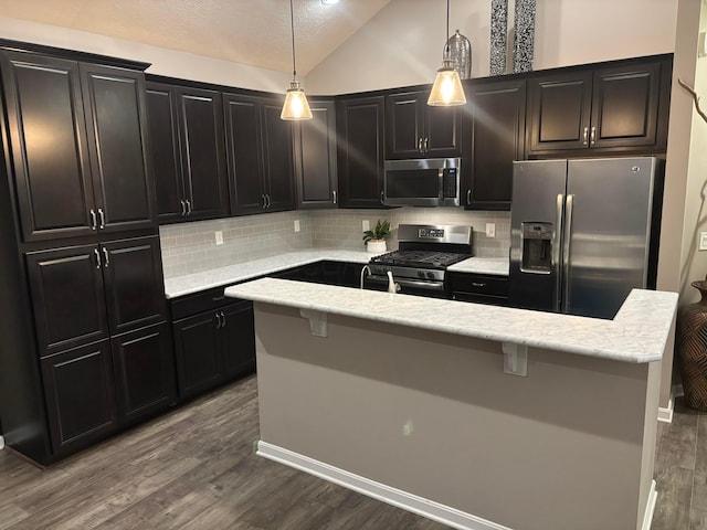 kitchen with pendant lighting, appliances with stainless steel finishes, hardwood / wood-style floors, a center island with sink, and vaulted ceiling