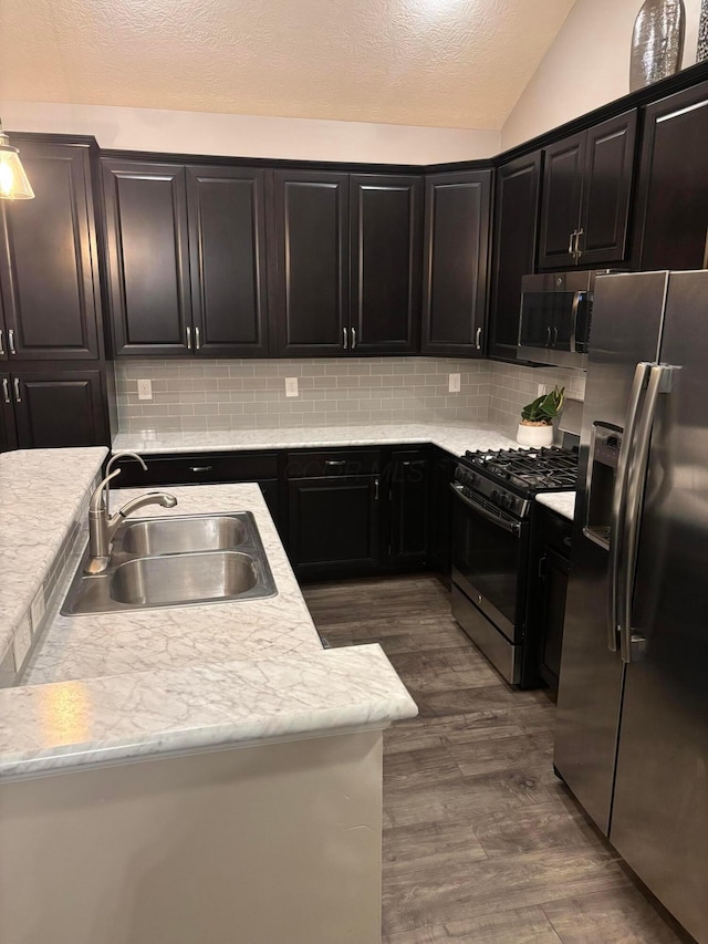 kitchen with sink, dark wood-type flooring, stainless steel appliances, tasteful backsplash, and vaulted ceiling