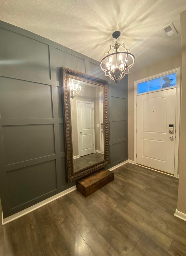 foyer entrance with dark hardwood / wood-style floors, a textured ceiling, and an inviting chandelier