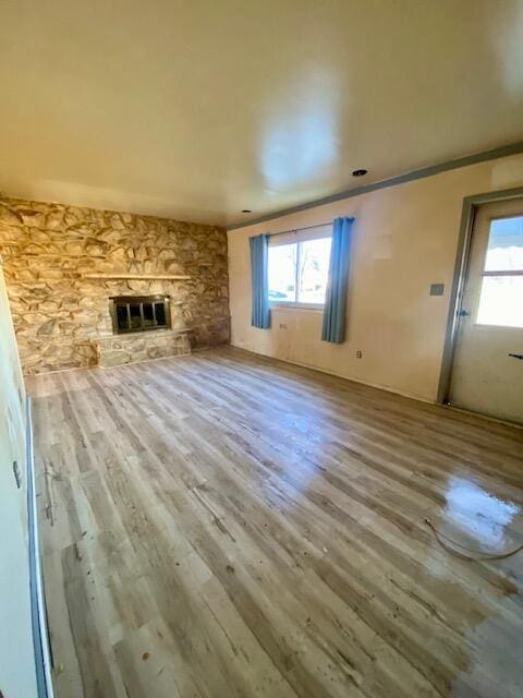 unfurnished living room featuring a stone fireplace, hardwood / wood-style floors, and ornamental molding