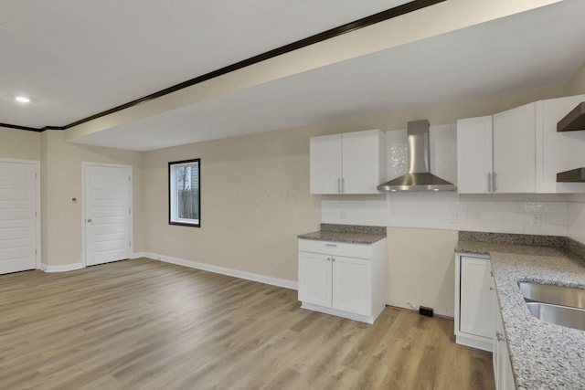 kitchen with backsplash, crown molding, wall chimney range hood, light hardwood / wood-style flooring, and white cabinets