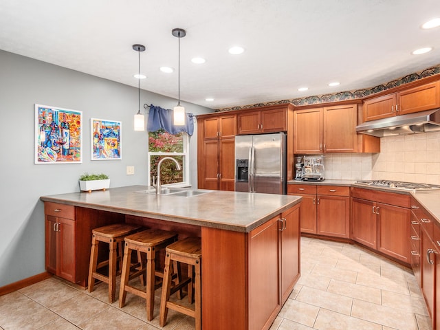 kitchen with sink, an island with sink, appliances with stainless steel finishes, decorative light fixtures, and a kitchen bar