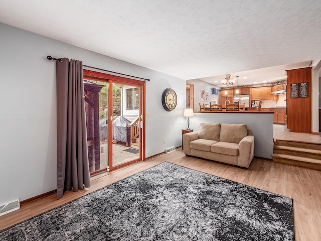 living room featuring a chandelier, a textured ceiling, and light hardwood / wood-style floors