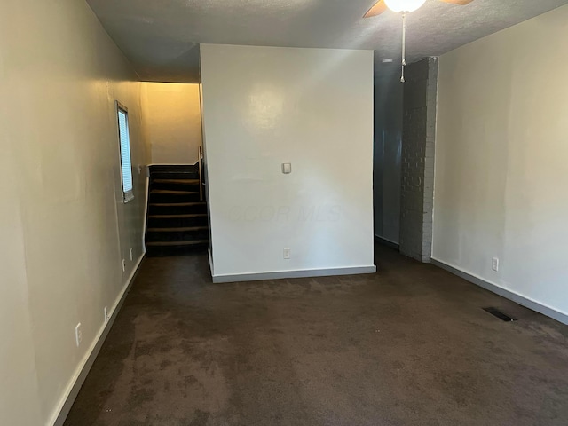 empty room with ceiling fan, a textured ceiling, and dark colored carpet