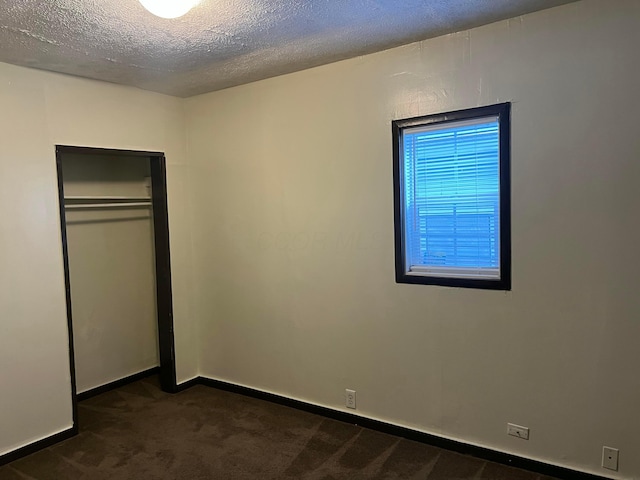 unfurnished bedroom featuring dark carpet, a textured ceiling, and a closet