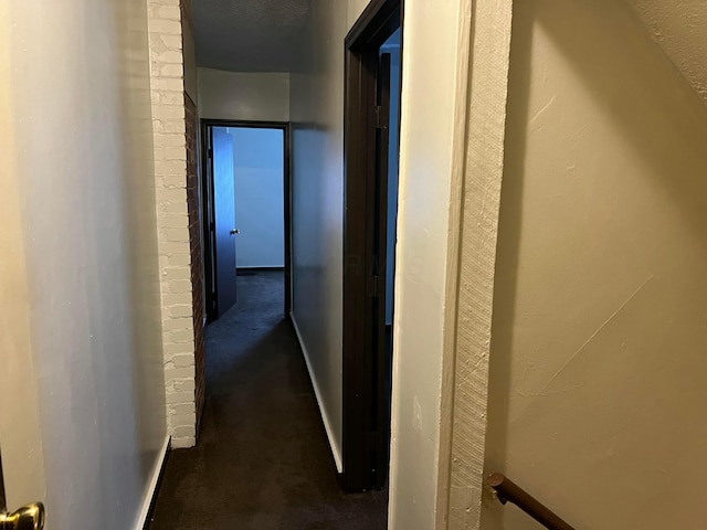 hallway featuring dark carpet and a textured ceiling