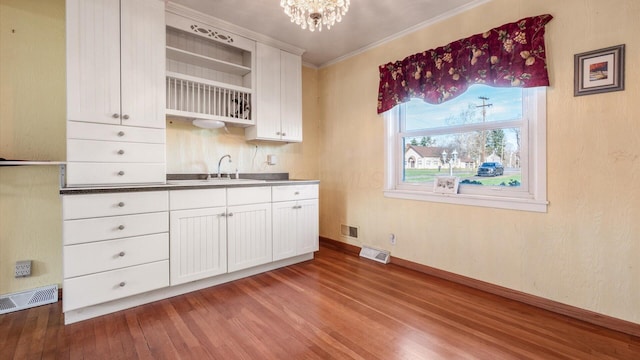 kitchen featuring white cabinets, wood-type flooring, ornamental molding, and sink