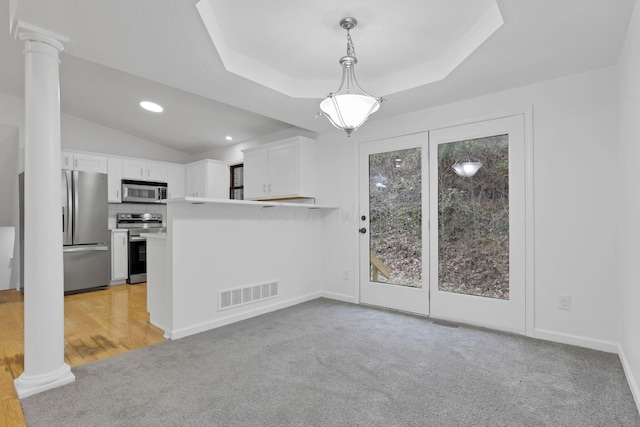 interior space with a raised ceiling, light colored carpet, and decorative columns